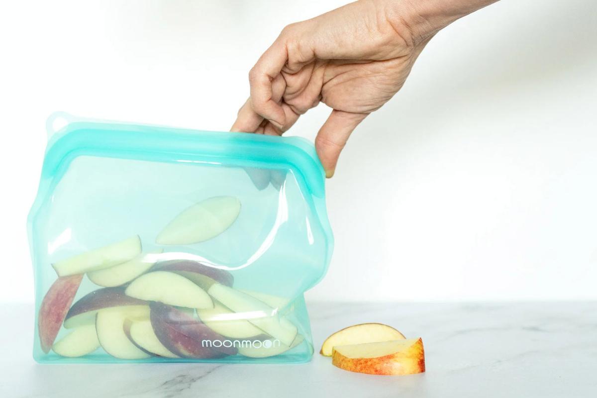 Blauer Silikonbeutel mit Apfelspalten, der von einer Hand geöffnet wird