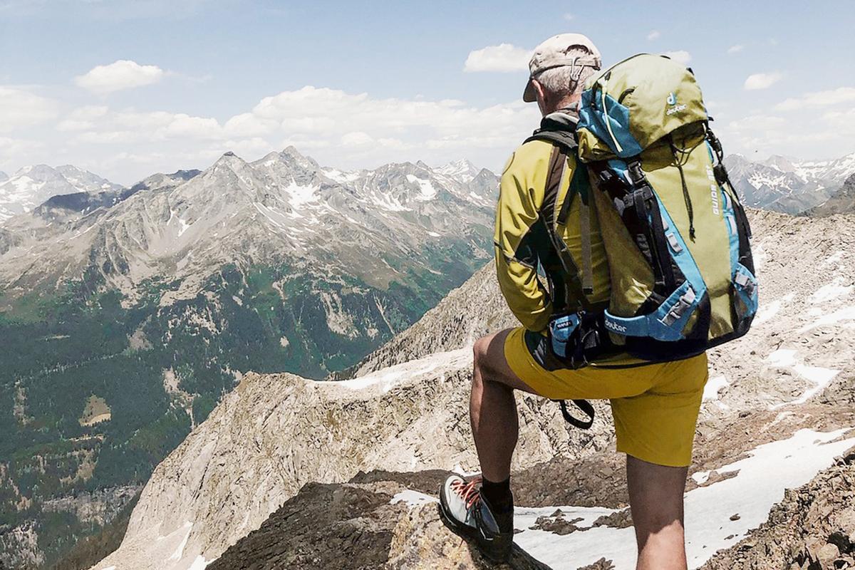 Ein Wanderer mit Rucksack - von hinten gesehen - der auf einem Berggipfel steht und in die Ferne schaut