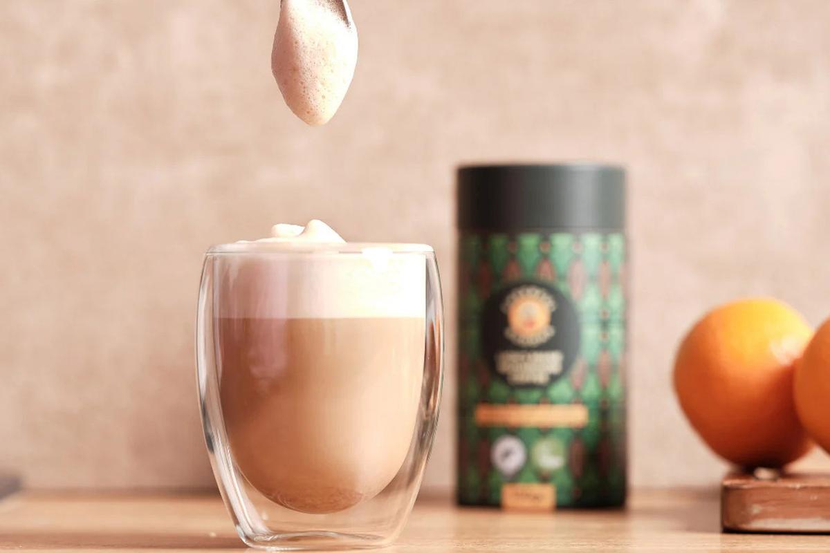 Lion's Mane Mushroom Coffee in der Verpackung. Links daneben steht ein Glas mit Kaffee und cremigem Schaum obendrauf.