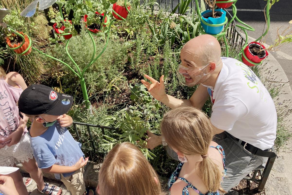 Apotheken-Workshop mit Sreco Dolanc, der in der Hocke vor dem Kräutergarten der Marien Apotheke Wien sitzt und Kindern verschiedene Kräuter erklärt