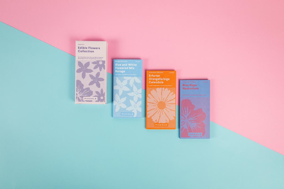 Rosa-hellblauer Hintergrund mit vier grafisch gestalteten Saatgut-Päckchen aus der "Essbare Blüten"-Kollektion von Piccolo Seeds