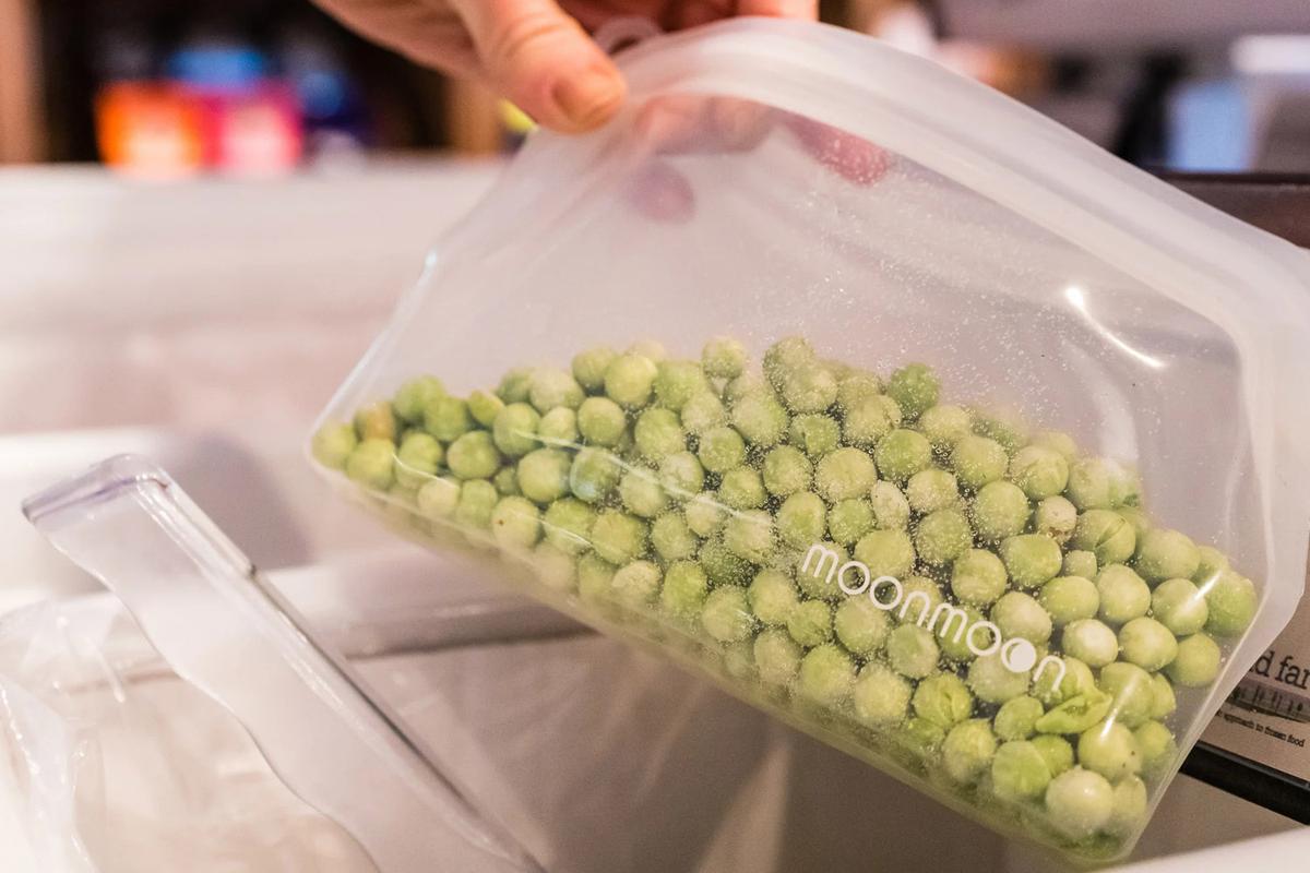 Rosa Silikonbeutel mit gefrorenen Erbsen, der über ein Abwaschbecken gehalten wird