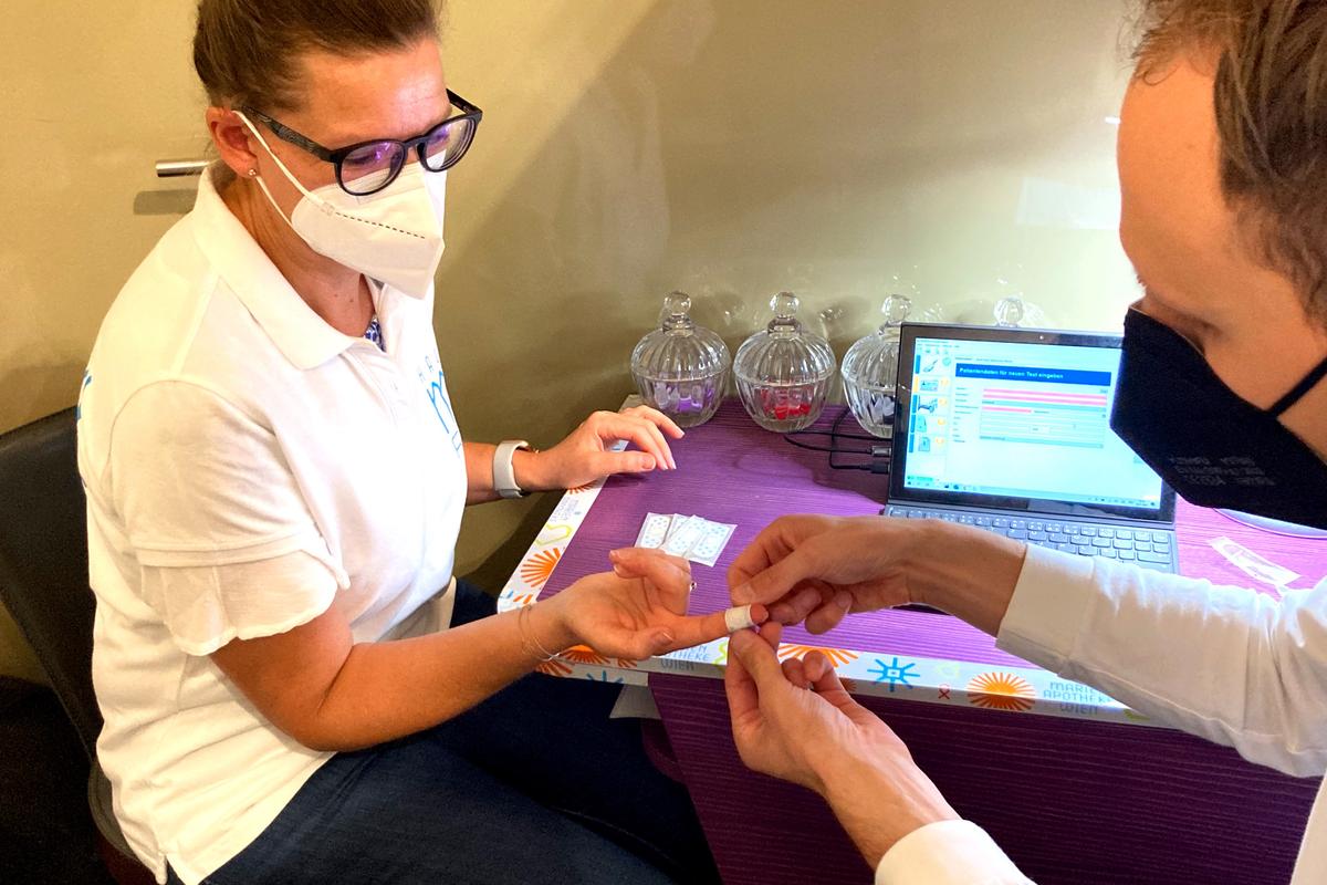 Frau die von einem Mann ein Pflaster auf einen Finger geklebt bekommt, nachdem ihr dort Blut abgenommen wurde für den FSME-Antikörper-Test in der Marien Apotheke