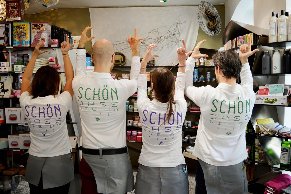 Mitarbeiter der Marien Apotheke in T-Shirts "Schön, dass Sie da sind" zeigen die Gebärde "COOL"