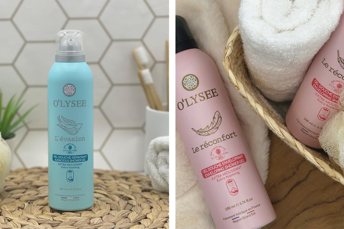 Zwei verschiedene Arten von Duschschaum von der Marke Olysée. Links steht eine türkise Sprühdose in einem Badezimmer, rechts liegt eine rosa Duschschaum-Sprühdose in einem Körbchen.