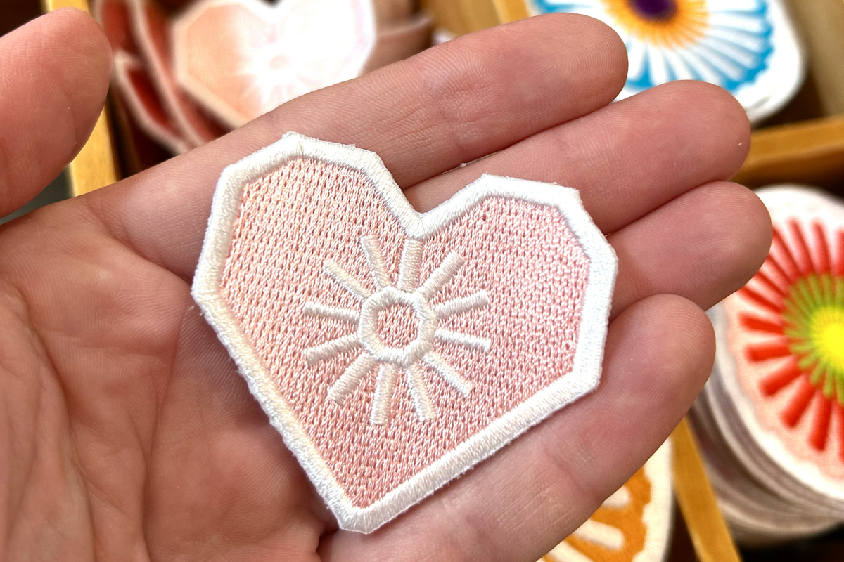 Rosa Aufnäher in Herzform mit dem Marienapotheken-Stern in der Mitte