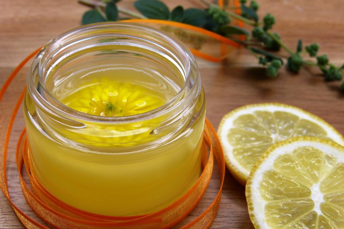 Ringelblumenblüte in einem durchsichtigen Cremetiegel mit danebenliegenden Zitronenscheiben